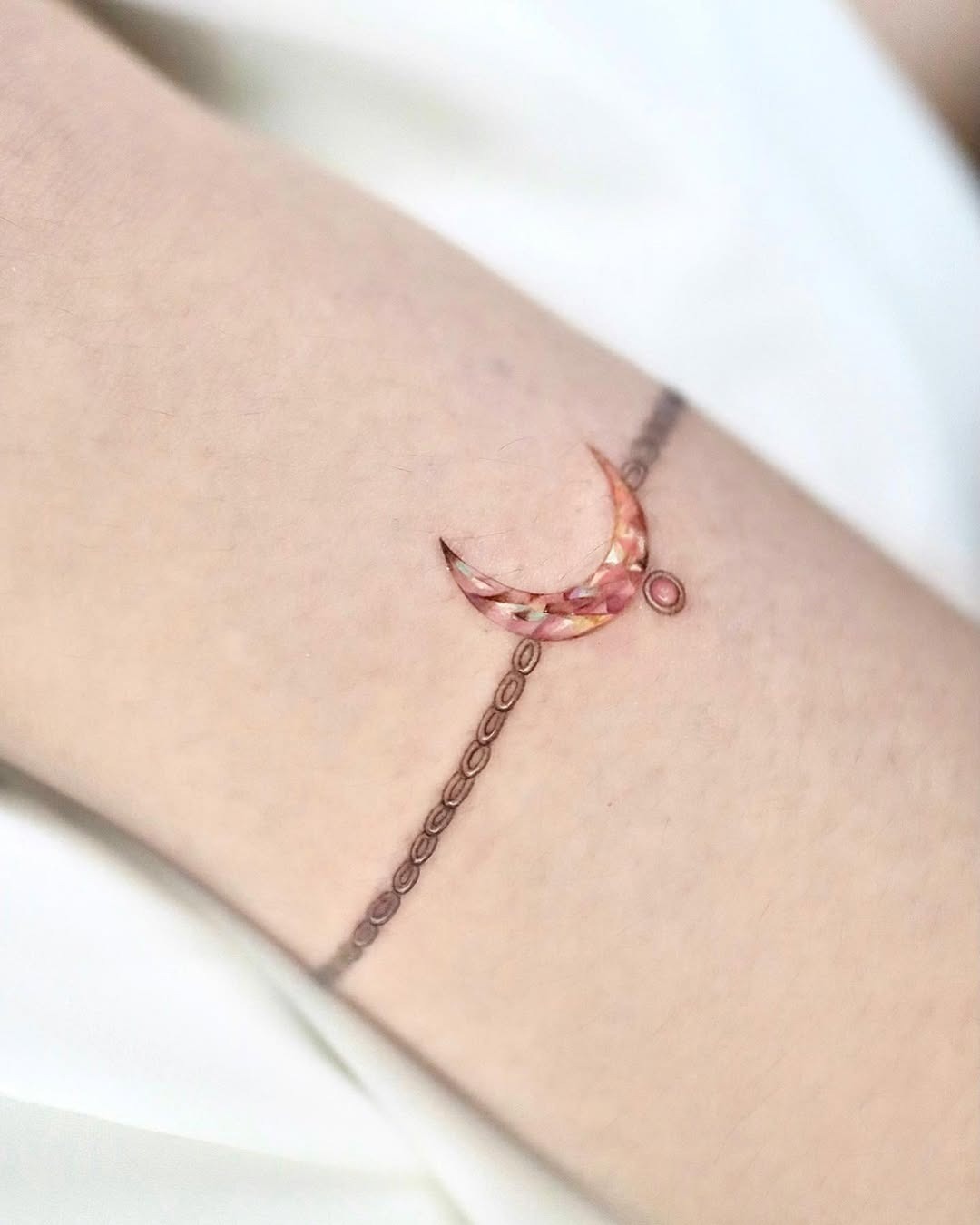 This delicate bracelet tattoo features a beautiful crescent moon adorned with intricate patterns.