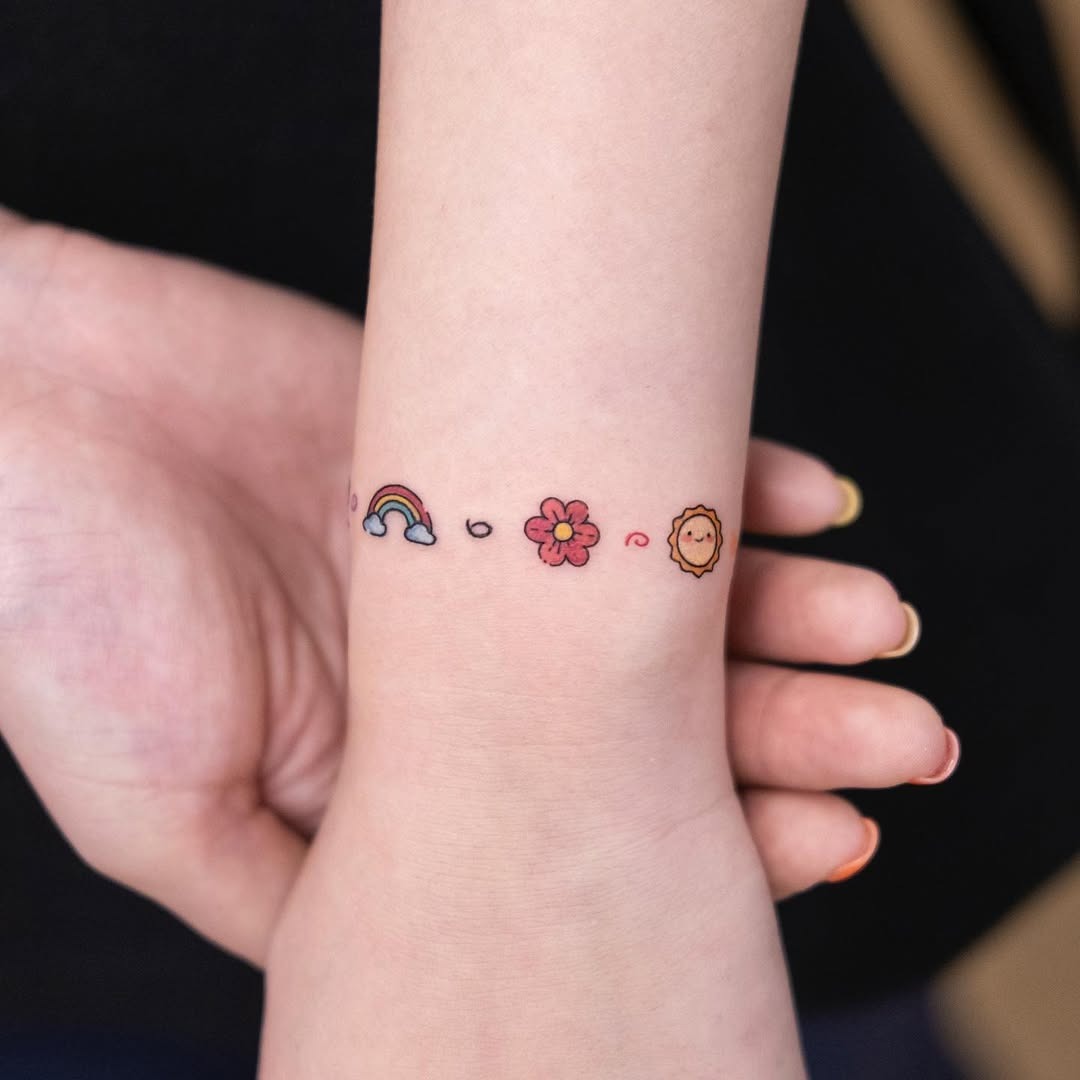 This charming bracelet tattoo features a playful sequence of a rainbow, flower, and lion.