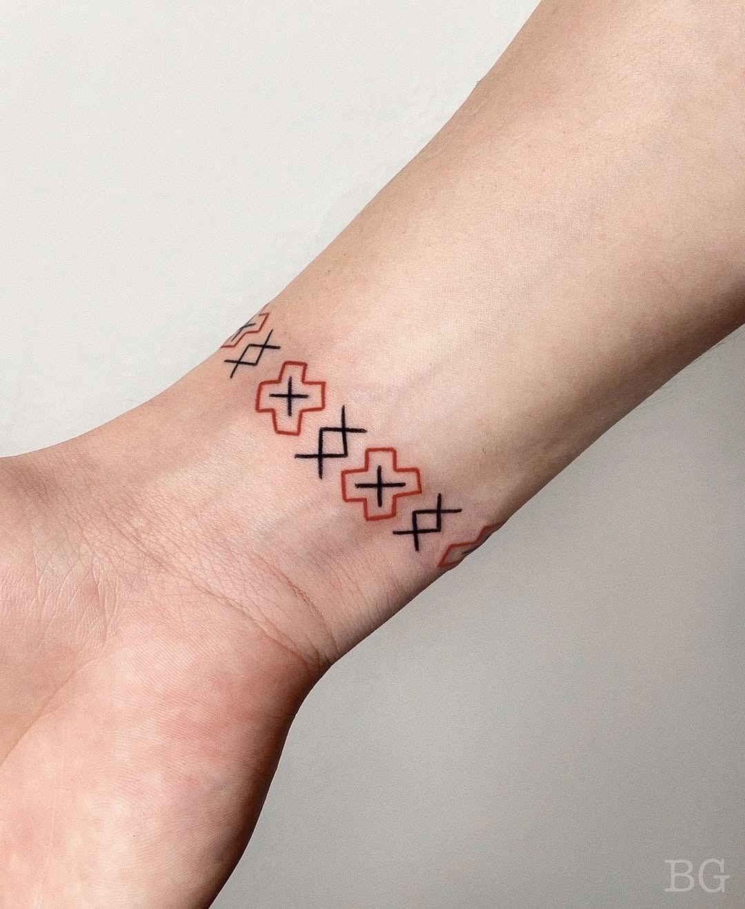 This tattoo features a series of geometric crosses wrapped around the wrist, creating a unique bracelet effect.