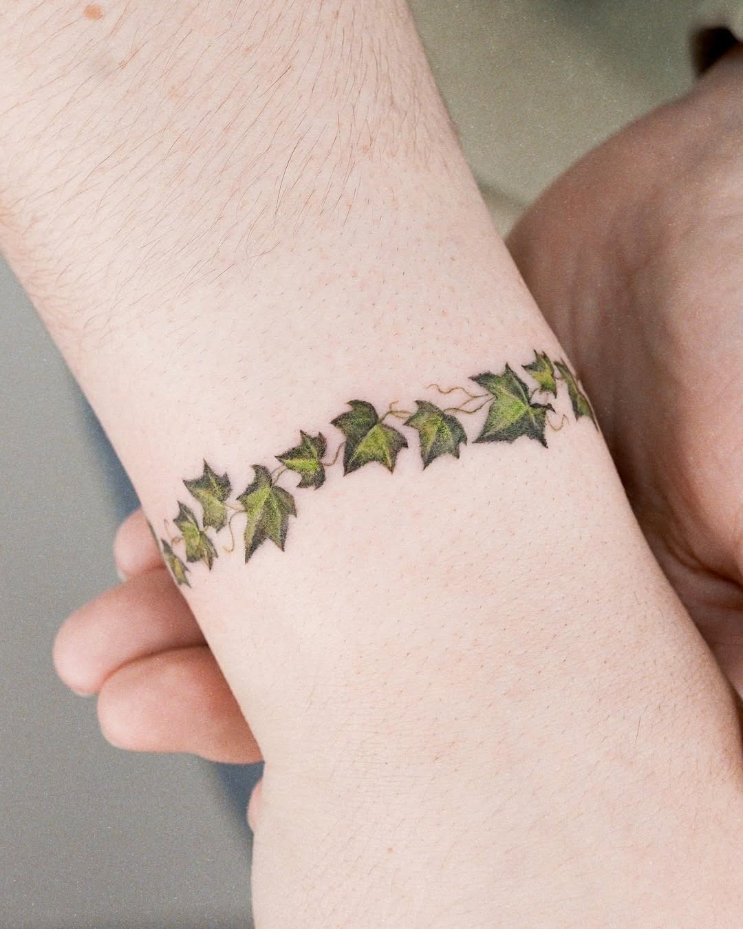 This charming tattoo features a series of green ivy leaves delicately entwined around the wrist, creating a natural bracelet effect.