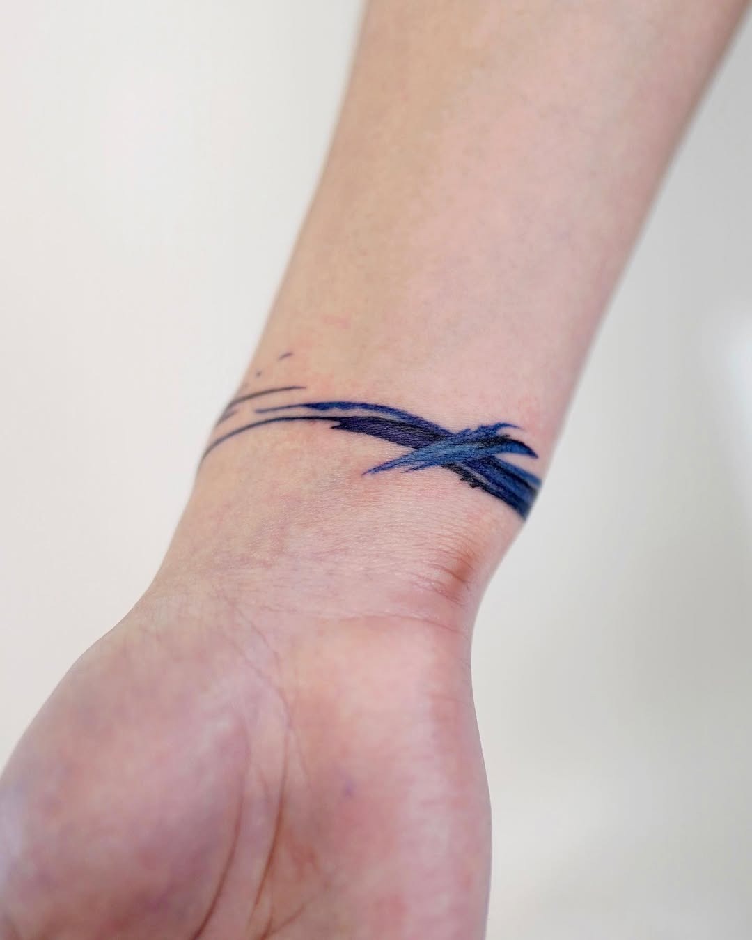 This tattoo features a fluid blue wave design around the wrist.