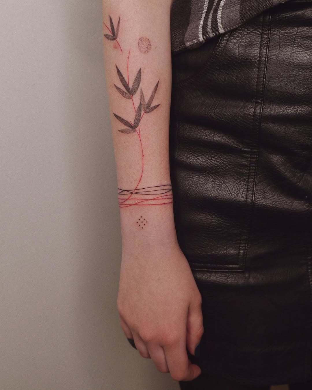 This tattoo features a delicate bamboo design that winds around the wrist, blending earthy greens with eye-catching red lines.