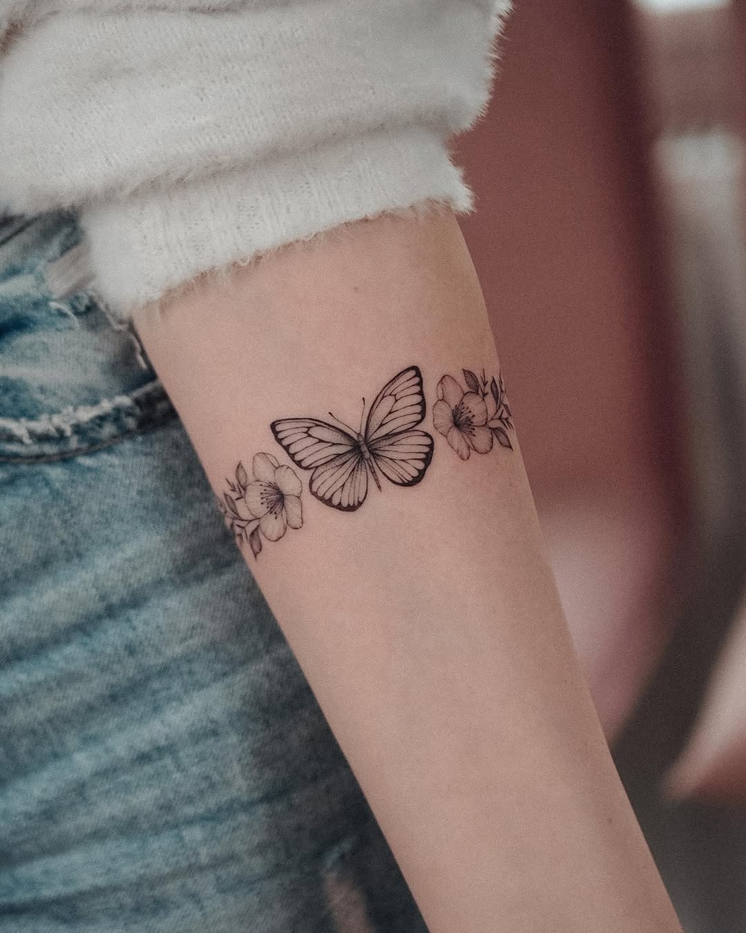 This delicate bracelet tattoo features a beautifully detailed butterfly surrounded by elegant flowers.