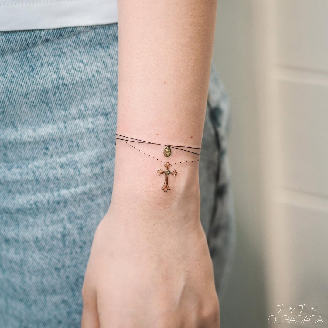 This tattoo features a delicate cross design connected by thin chains, giving it a bracelet-like appearance on the wrist.