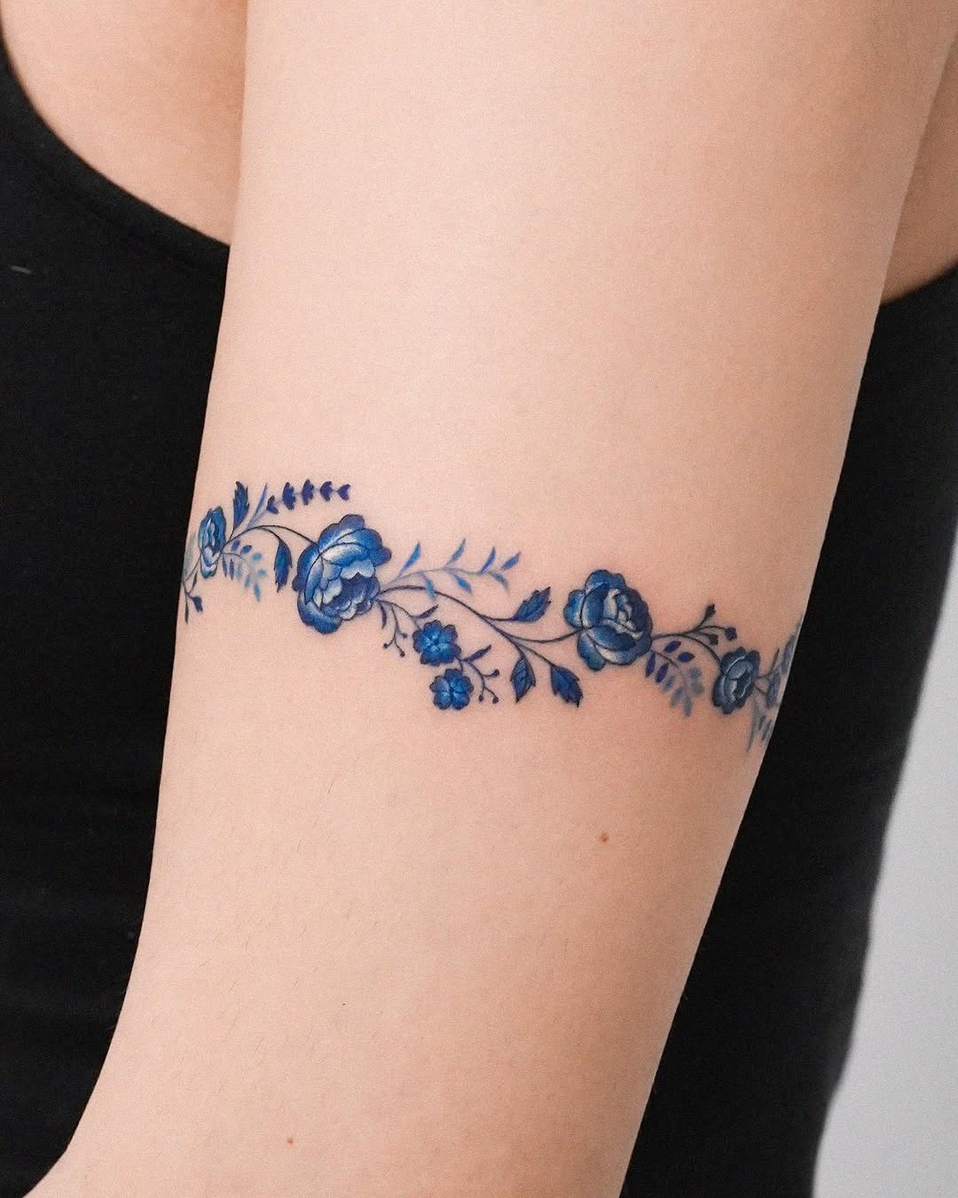 This beautiful bracelet tattoo features delicate blue roses intertwined with smaller floral designs.