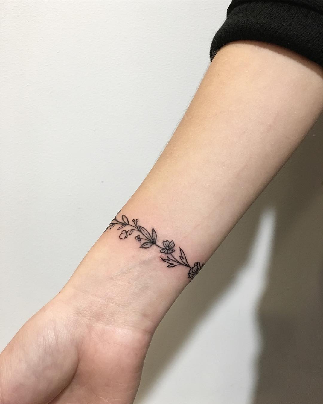 This tattoo showcases a delicate design of flowers and leaves wrapped around the wrist.