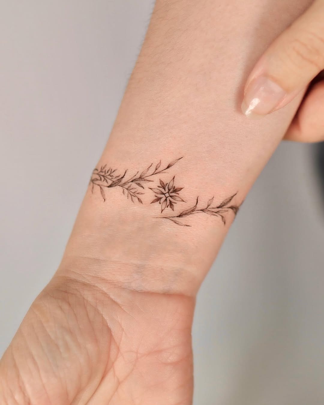 This lovely wrist tattoo features delicate flowers and leaves, showing a minimalistic design.
