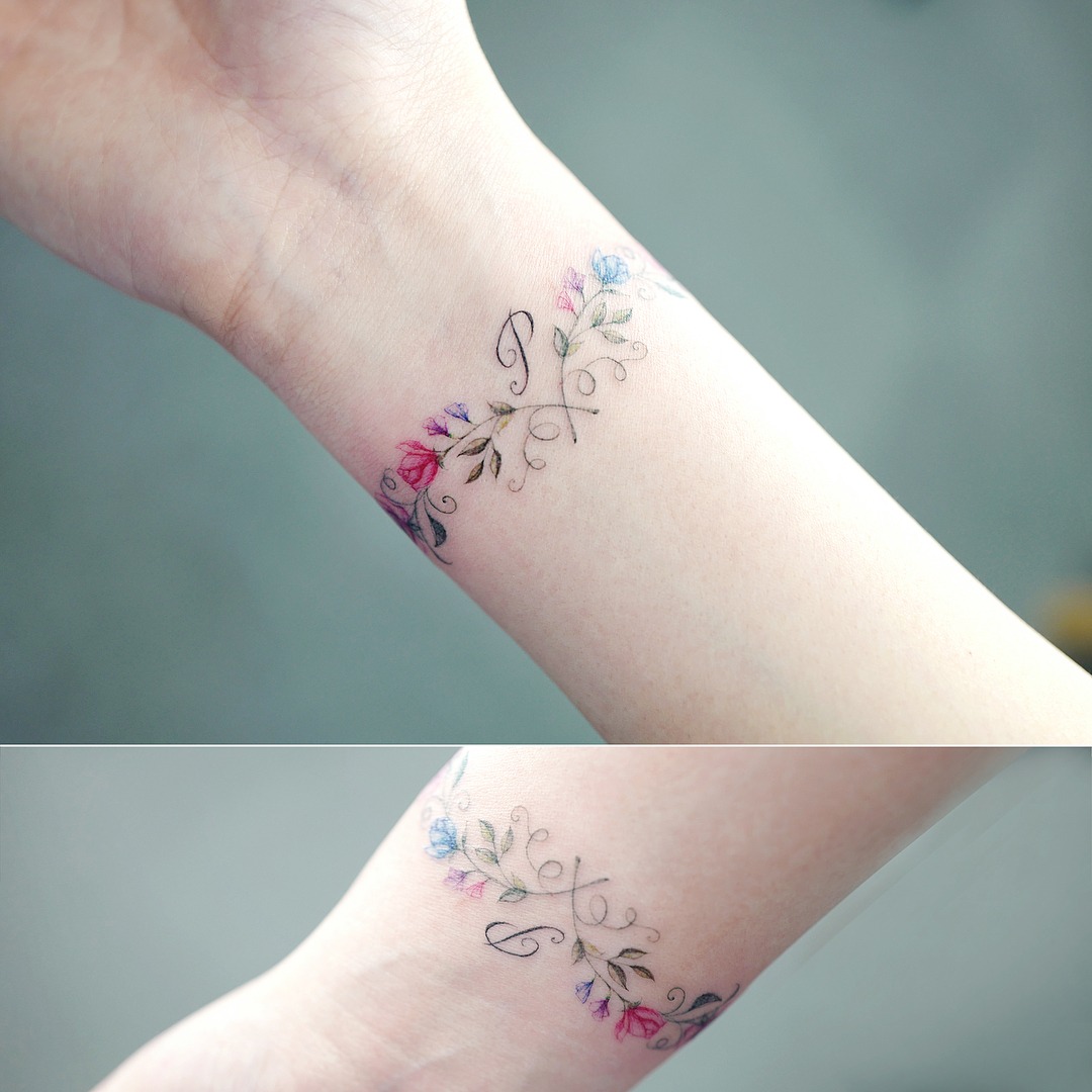 This delicate bracelet tattoo features beautiful floral elements intertwined with elegant swirls.