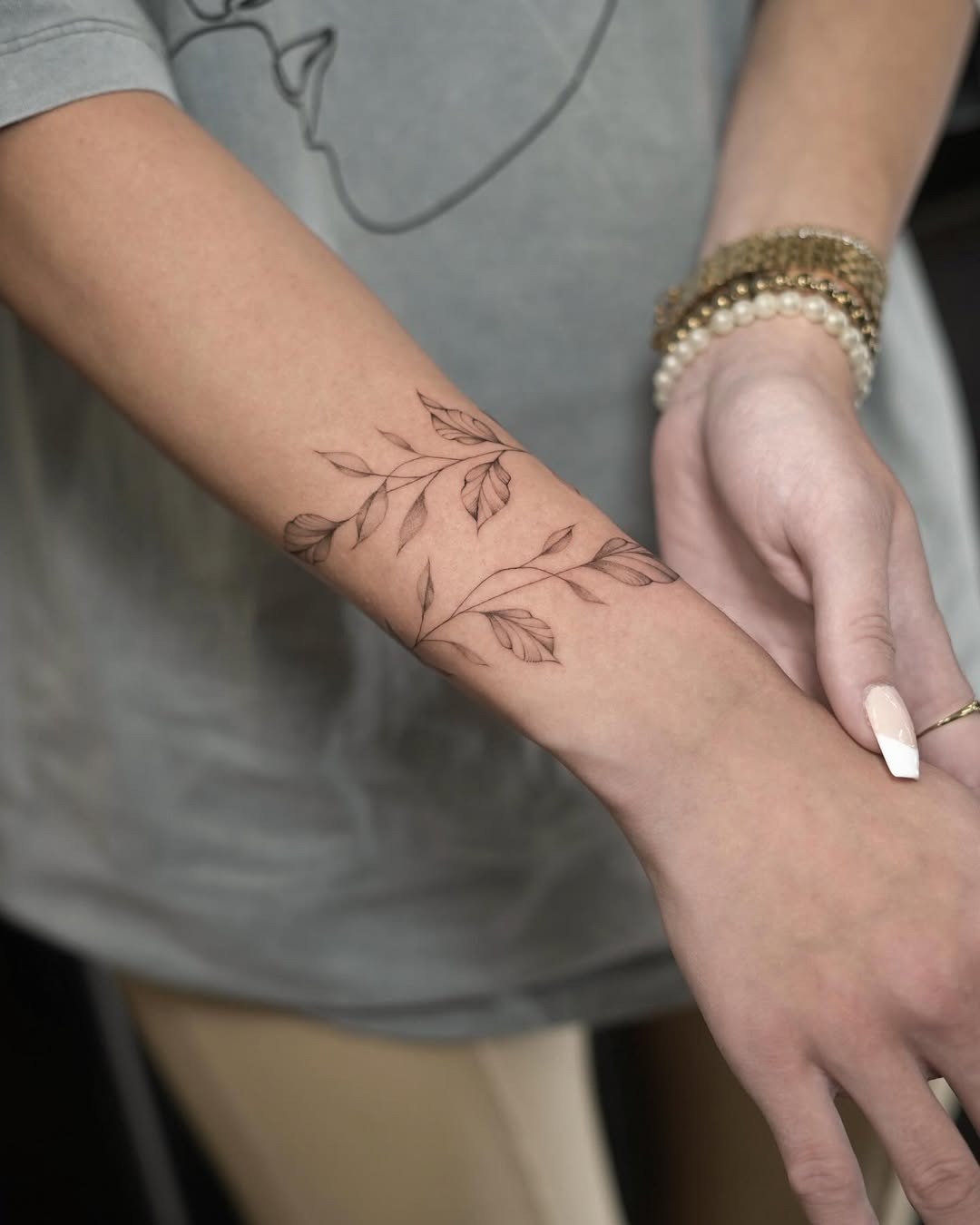 This tattoo features delicate leaves intertwined around the wrist, resembling a bracelet.