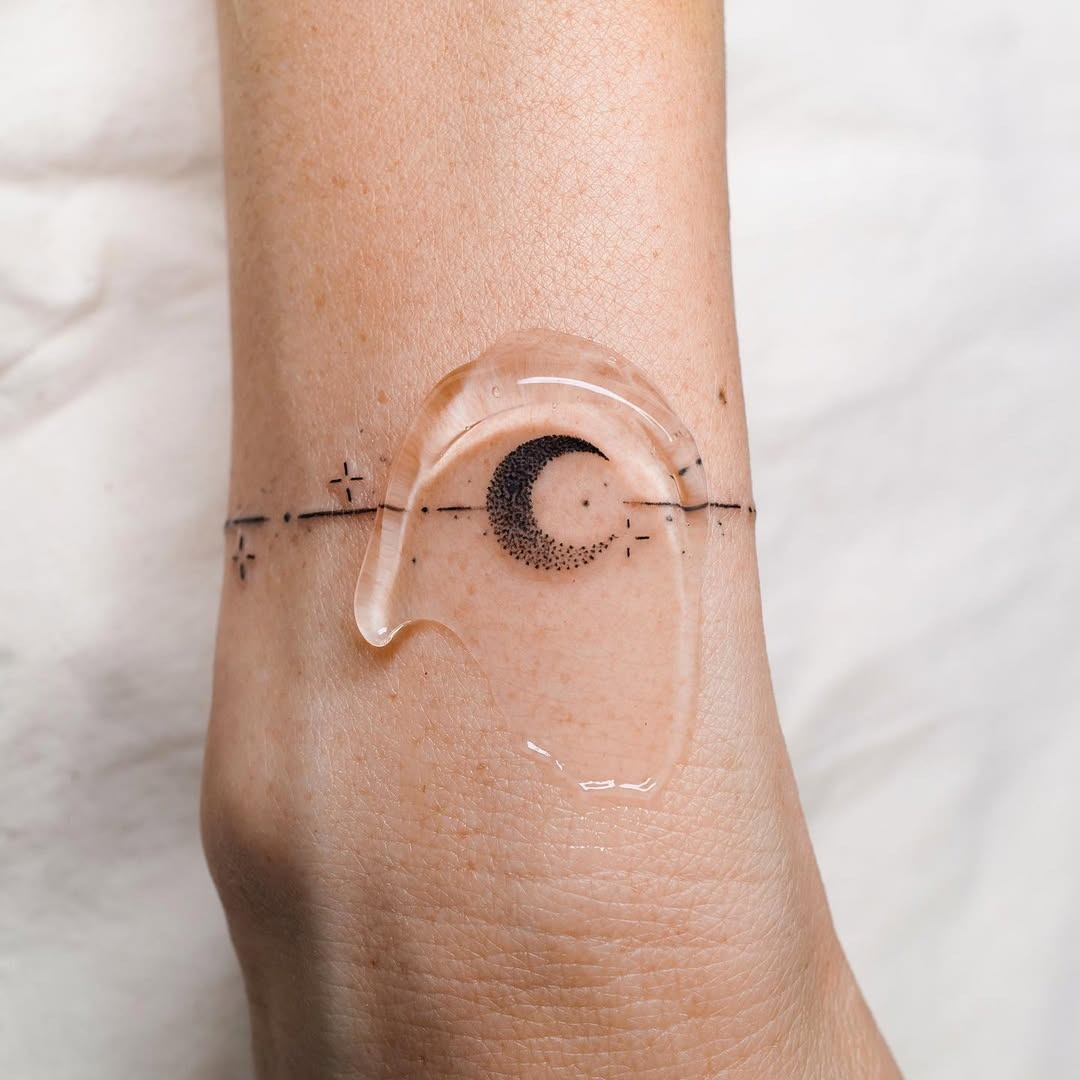 This tattoo features a delicate moon paired with tiny stars, wrapped around the wrist.