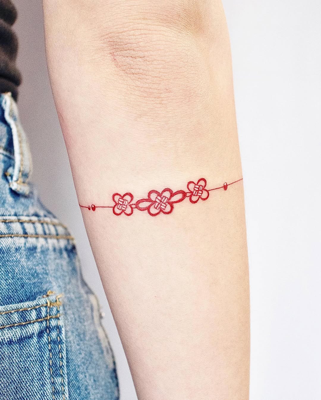 This minimalist bracelet tattoo features a delicate design of interlinked red flowers.