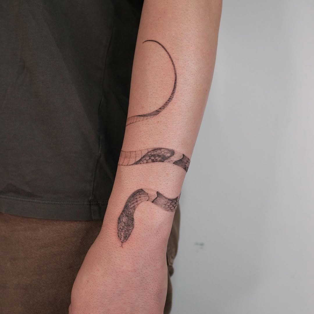 This tattoo features a beautifully flowing snake design wrapping around the forearm.