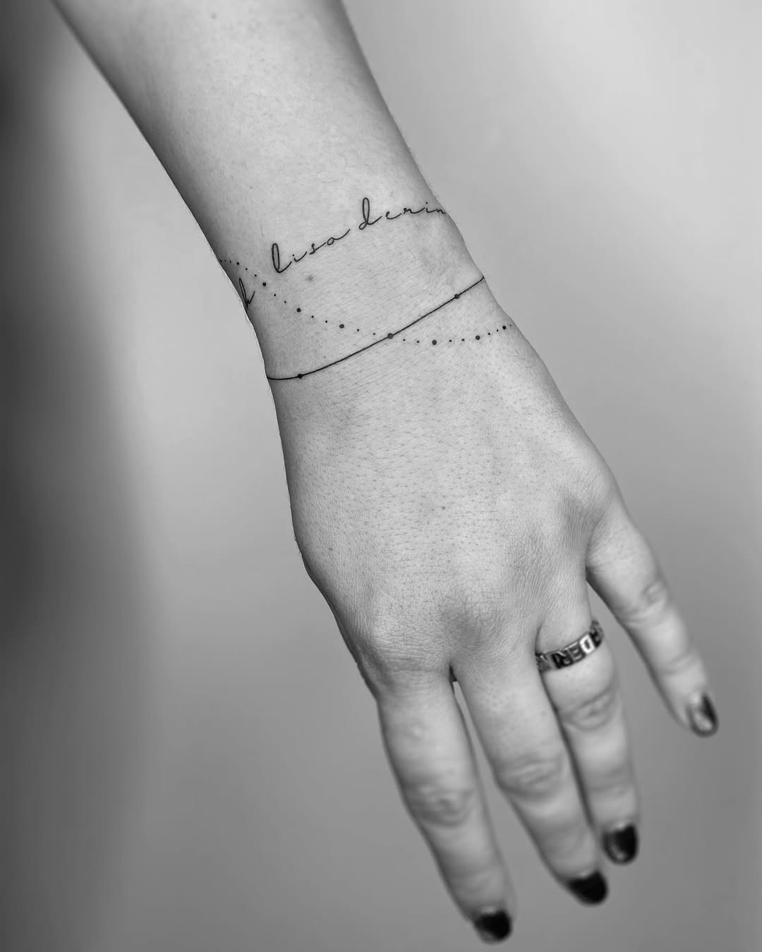 This tattoo features a delicate script intertwined with a dotted line, elegantly wrapping around the wrist.