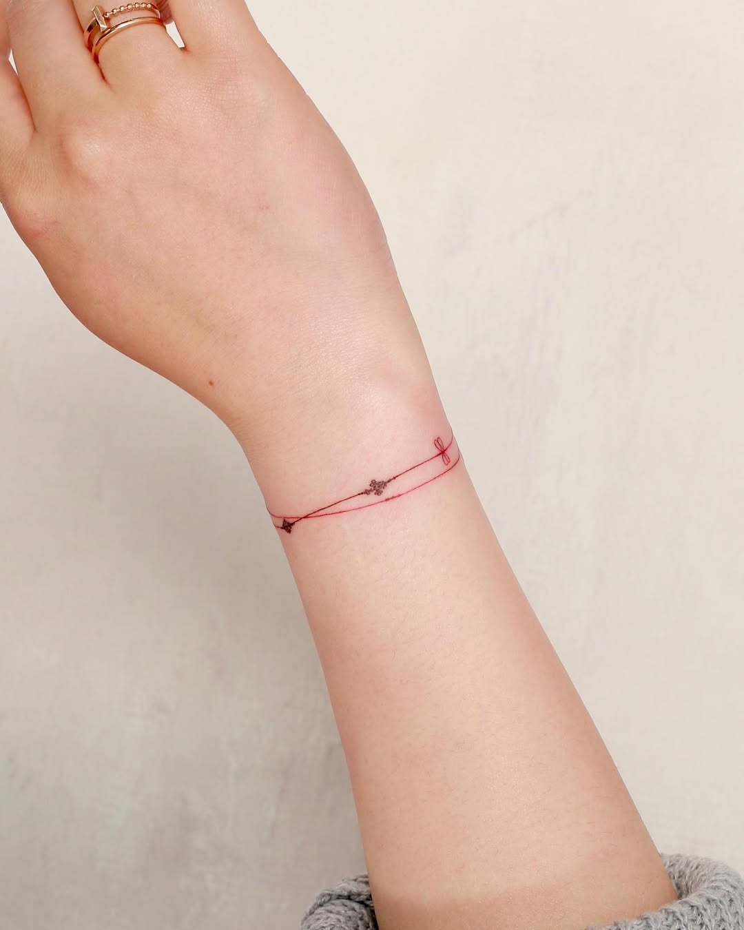 This tattoo features a delicate red line wrapped around the wrist, creating a subtle bracelet effect.