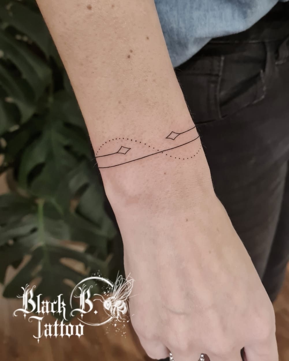 This tattoo features a delicate bracelet design with thin black lines interconnected by small diamond shapes and dotted accents.