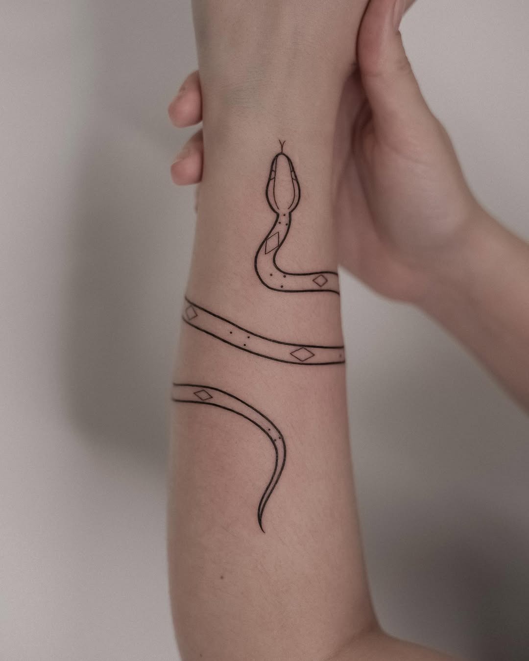 This minimalist bracelet tattoo features a beautifully drawn snake coiling gracefully around the wrist.