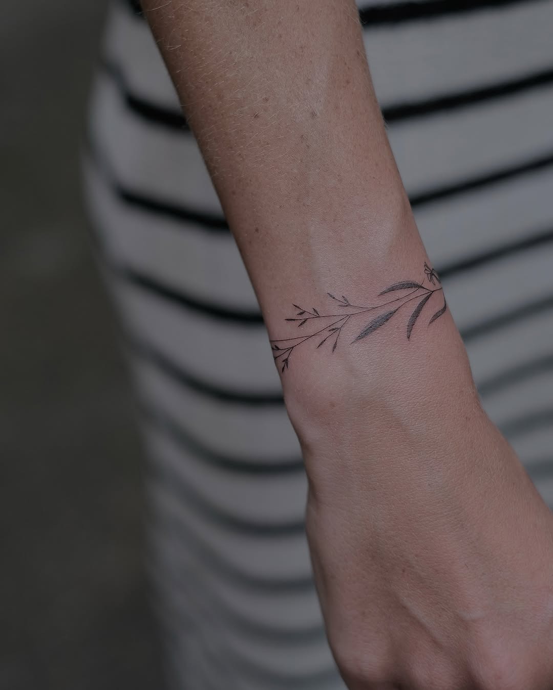 This tattoo features a minimalist floral design wrapping around the wrist, giving it a natural, earthy vibe.