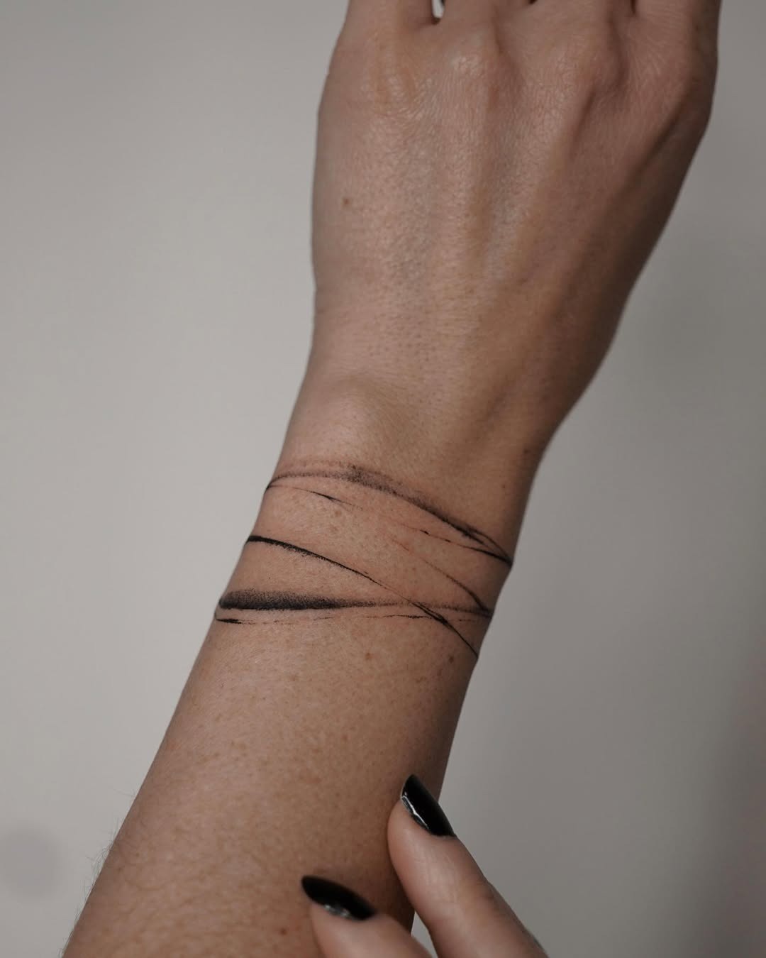 This tattoo features a minimalistic design with three bold black lines wrapping around the wrist.