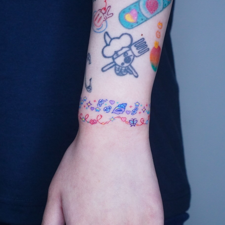 This tattoo features a bracelet design adorned with colorful elements and whimsical patterns.