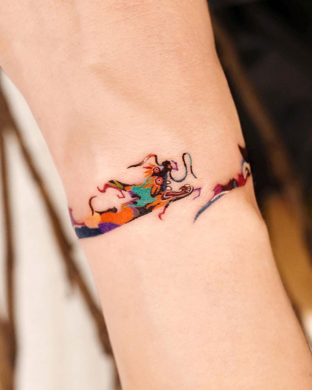 This colorful bracelet tattoo features a whimsical dog design that flows beautifully around the wrist.