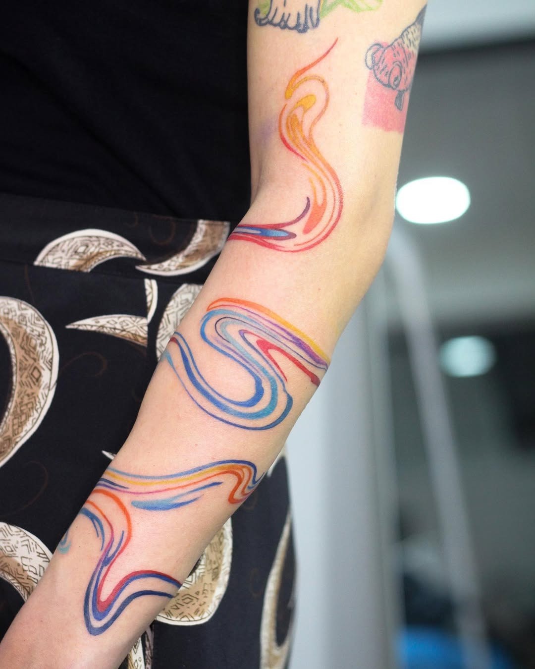 This tattoo features a colorful swirl design wrapping around the arm, creating a dynamic visual effect.