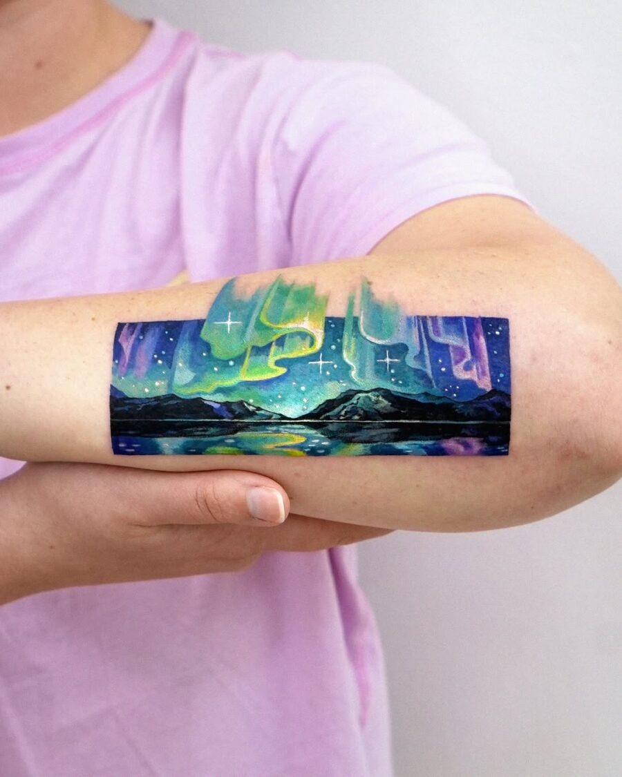 This stunning tattoo features a depiction of northern lights set against a serene landscape.