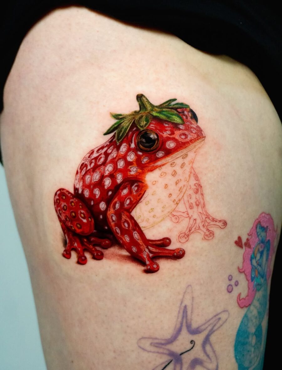 This colorful tattoo showcases a striking red strawberry frog, bursting with hues.