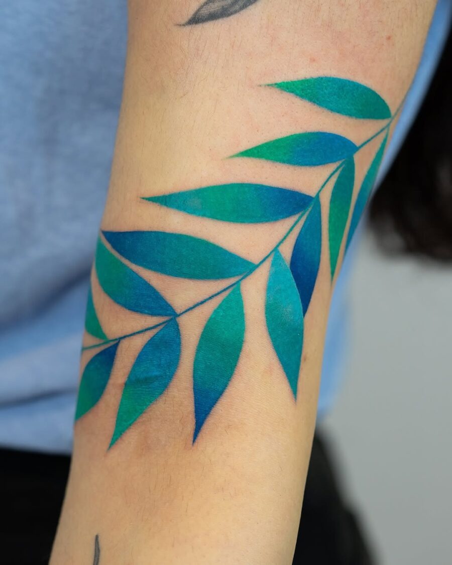 This leaf tattoo showcases a beautiful blend of green and blue hues that really pop.