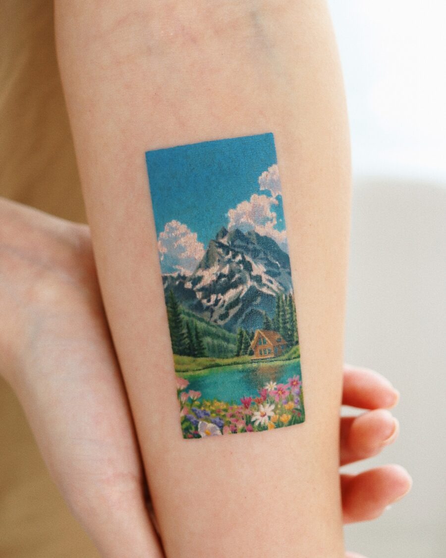 This stunning tattoo showcases a mountain scene with bright colors and beautiful flowers.