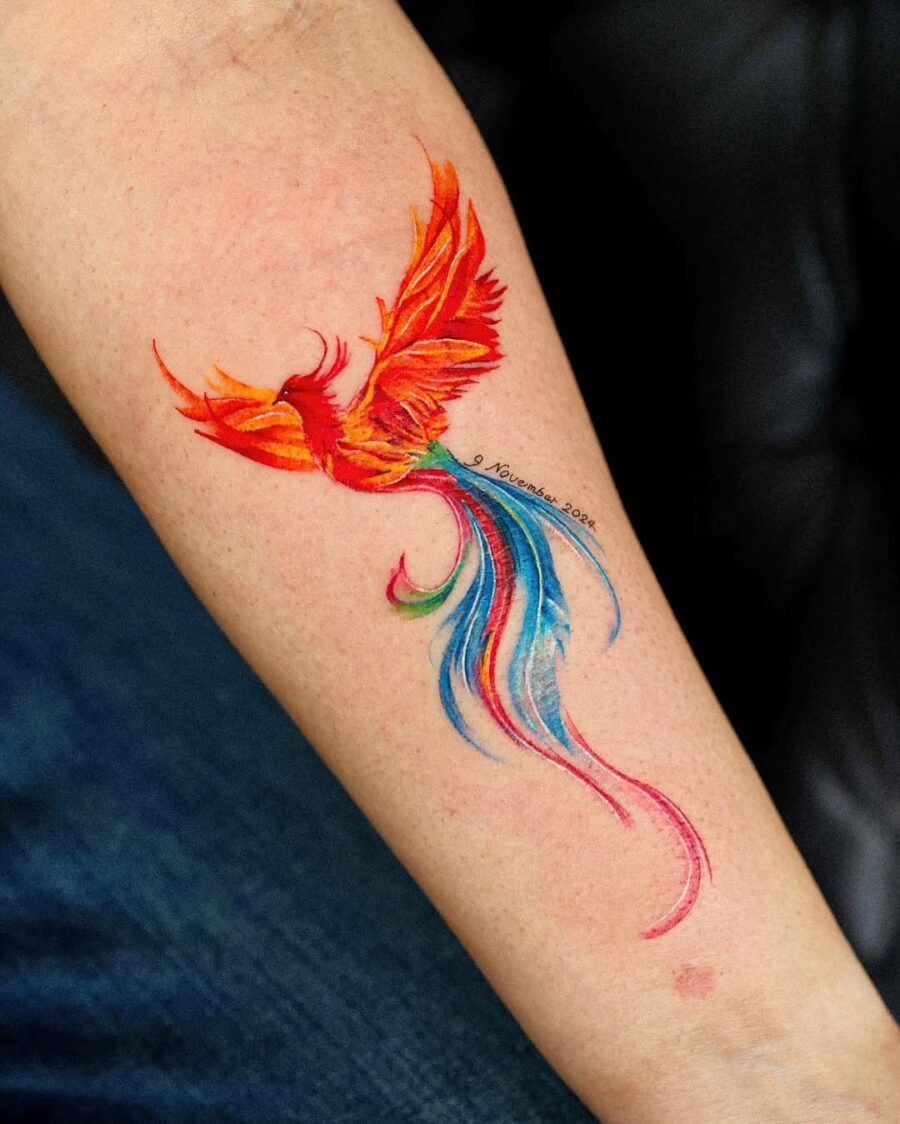 This bright phoenix tattoo bursts with fiery orange and stunning blue hues, embodying a sense of freedom and transformation.