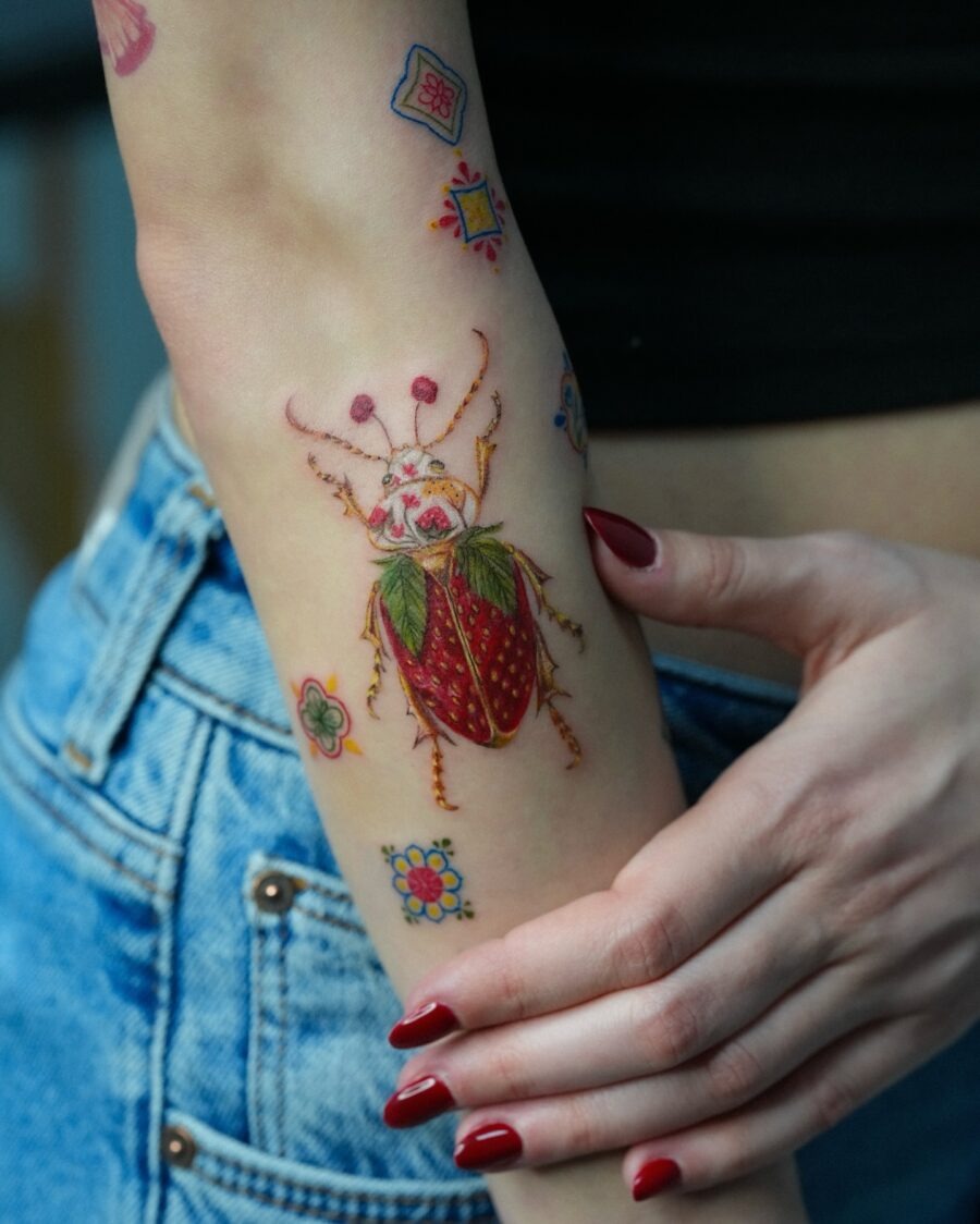 This tattoo features a colorful beetle adorned with floral elements, showing a lively design.