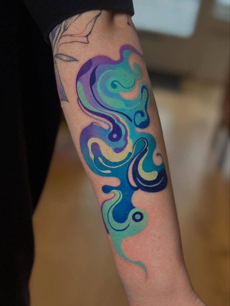 This bright color tattoo features a whimsical wave design, filled with shades of turquoise, purple, and blue.
