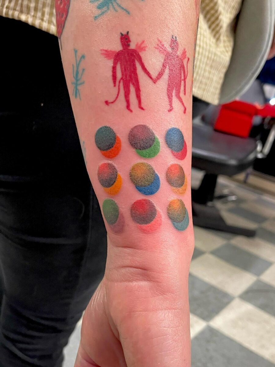 This tattoo features two whimsical characters, one red and one light, holding hands.