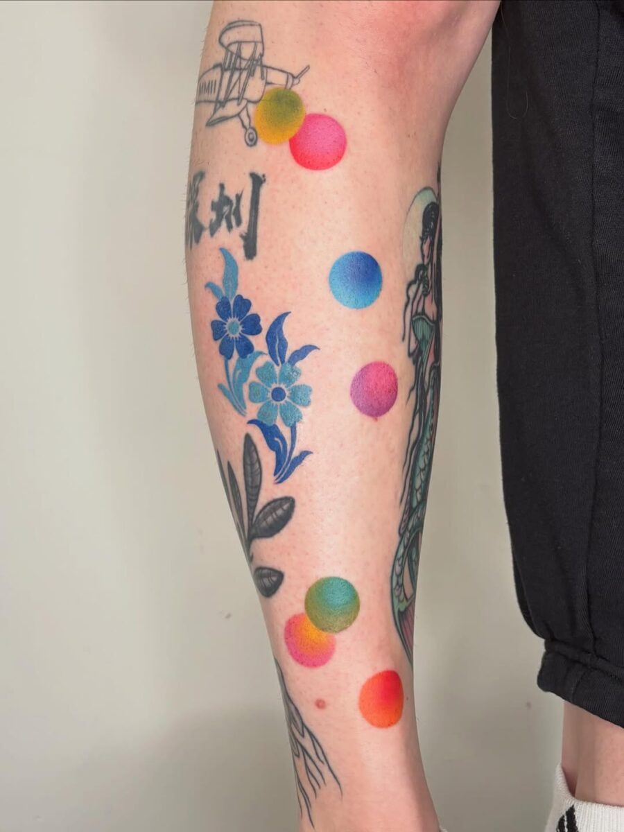 This arm tattoo showcases a mix of playful colorful designs, adding a bright twist to traditional ink art.