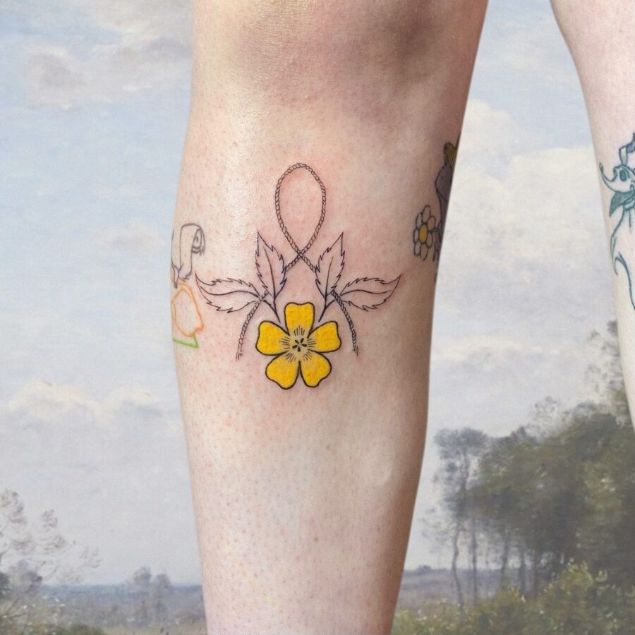 This delicate buttercup flower tattoo beautifully adorns the leg with its yellow petals.
