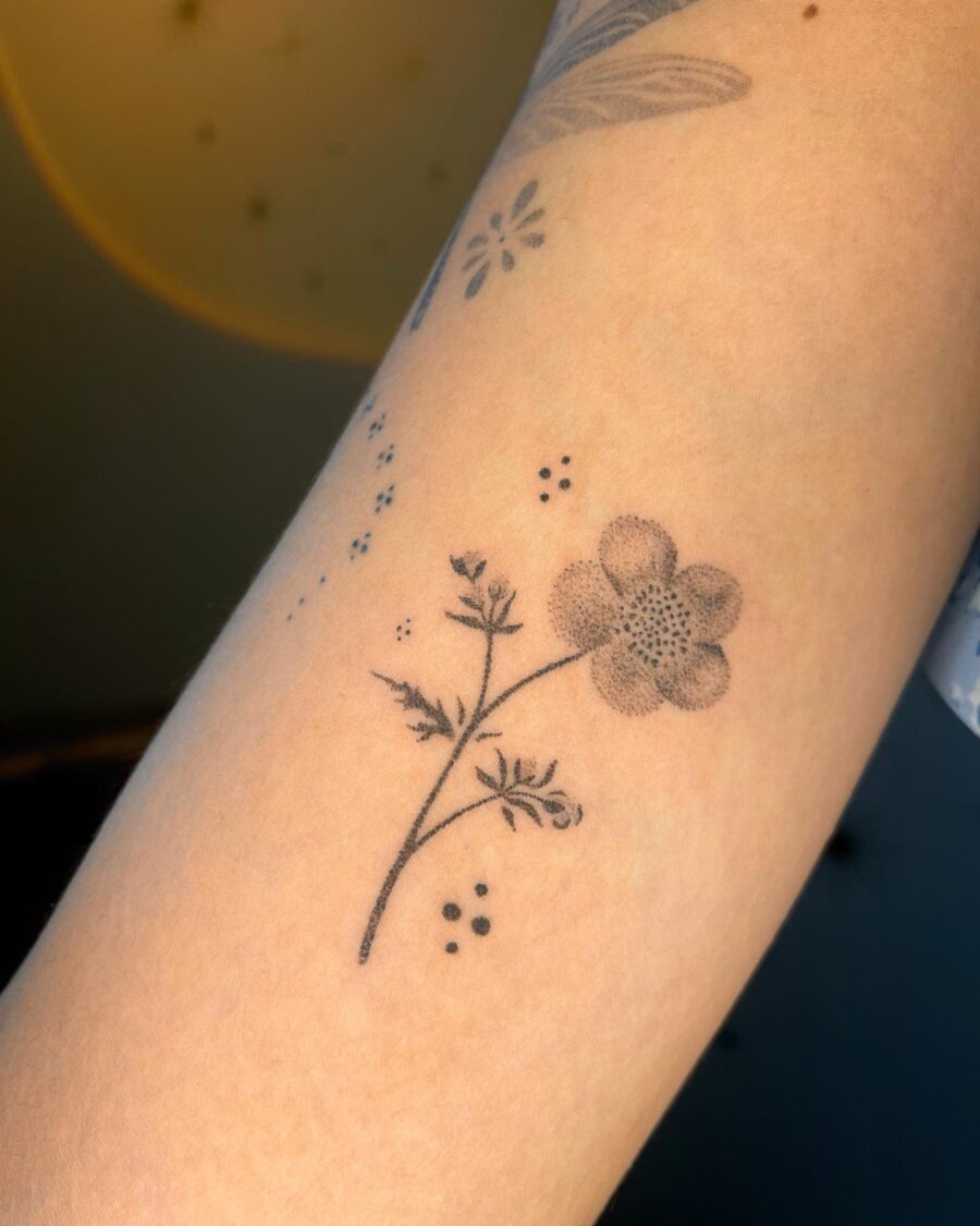 This minimalist buttercup flower tattoo showcases delicate lines and fine dotting.
