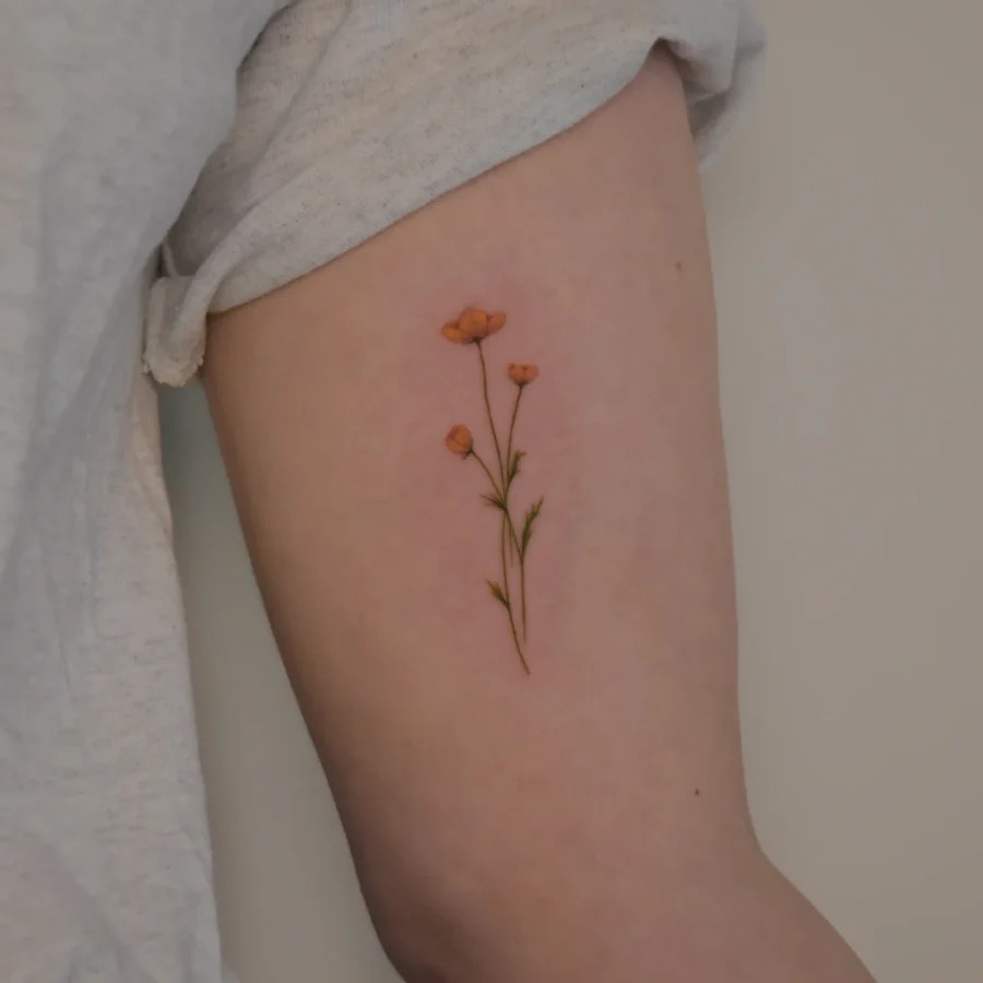 This tattoo features delicate buttercup flowers gracefully placed on the upper arm.