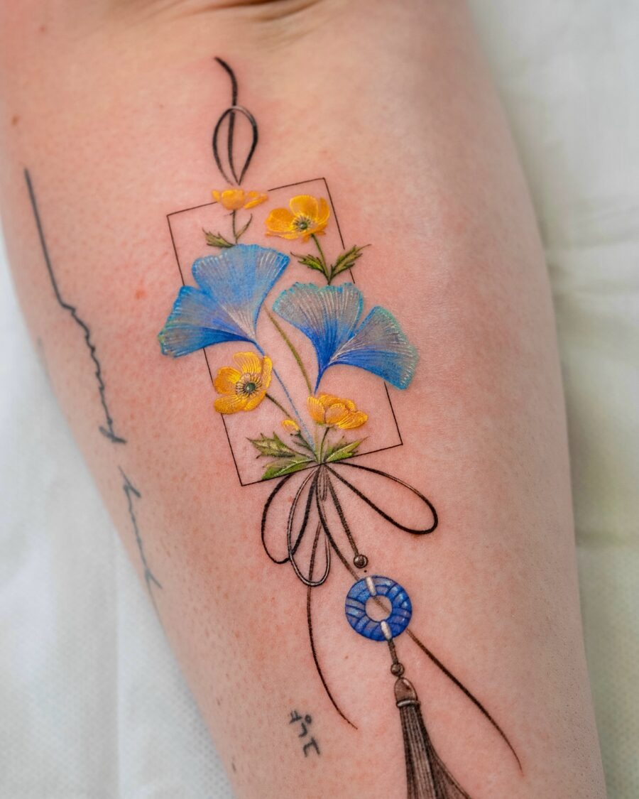 This tattoo beautifully showcases blue and yellow buttercup flowers intertwined with delicate black lines.