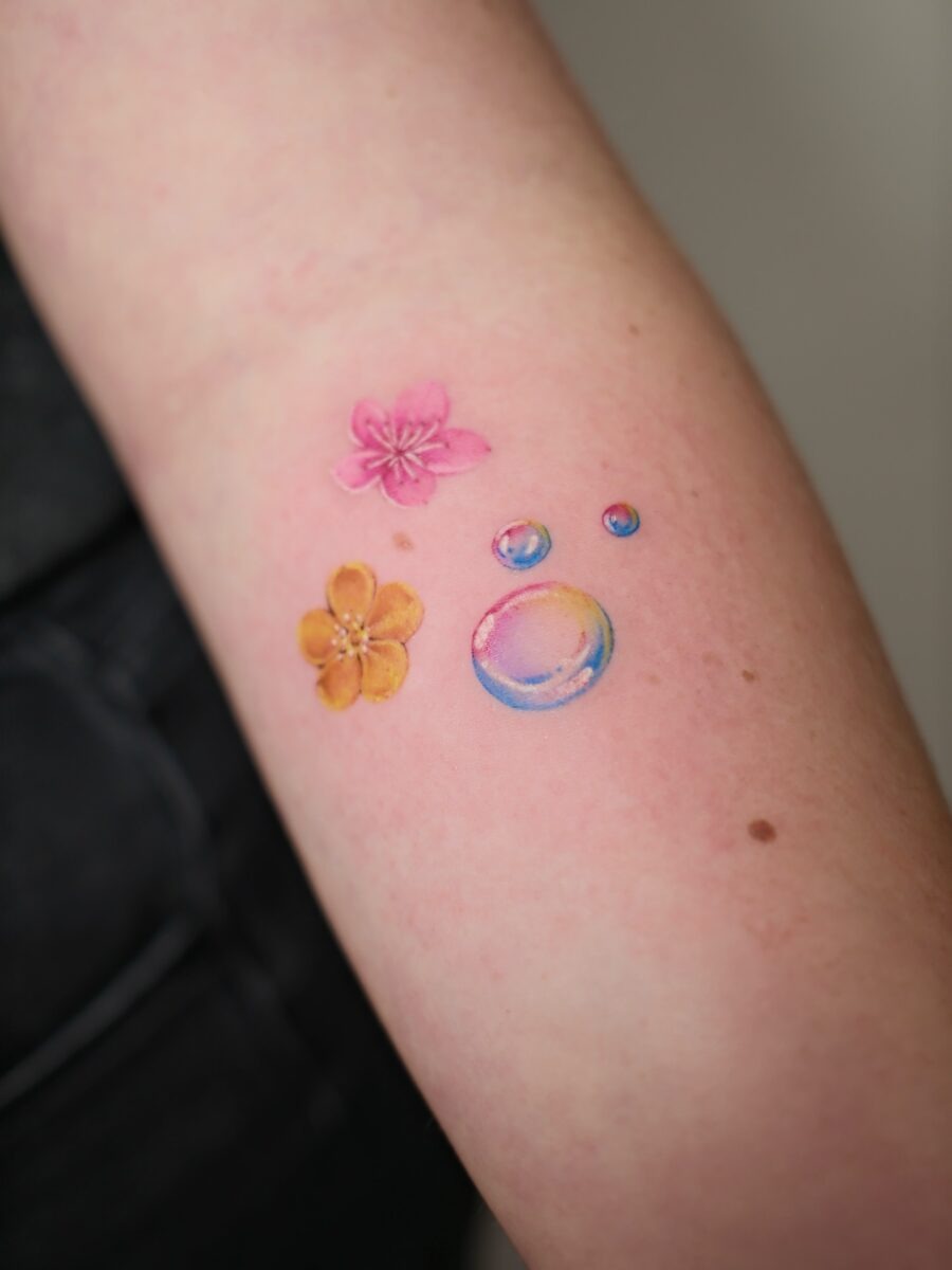 This tattoo features a delightful buttercup flower paired with colorful bubbles.