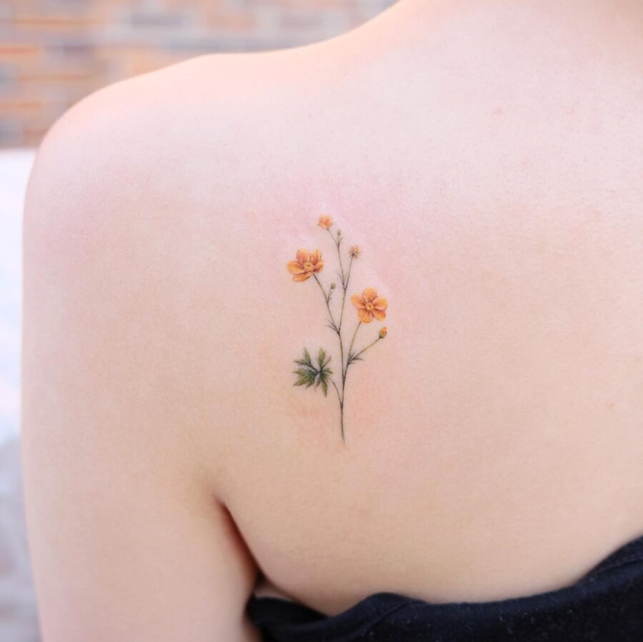 This delicate buttercup flower tattoo features soft orange blooms and lush green leaves, beautifully inked on the shoulder.