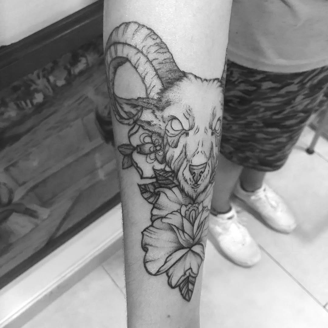 This striking tattoo features a detailed ram's head paired with elegant flowers.