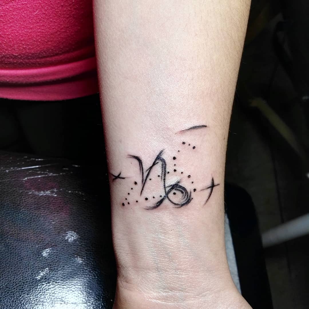 This minimalist Capricorn tattoo features the zodiac sign's symbol intertwined with delicate dots and stars.
