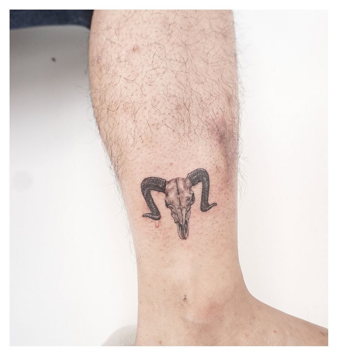 This tattoo features a striking ram skull with curling horns intertwined with a snake.
