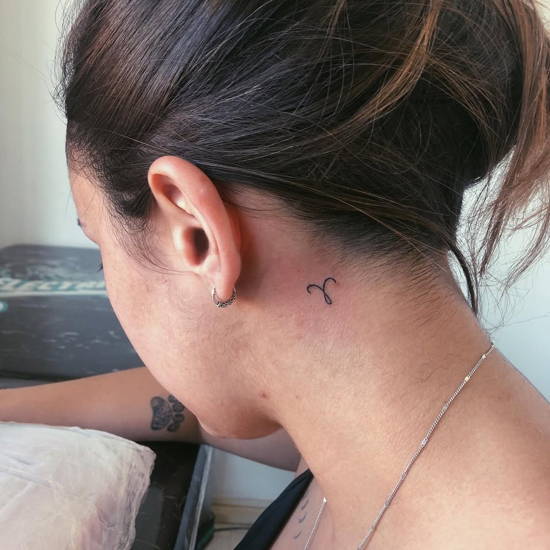 This minimalist Capricorn tattoo features a sleek design, subtly placed behind the ear.