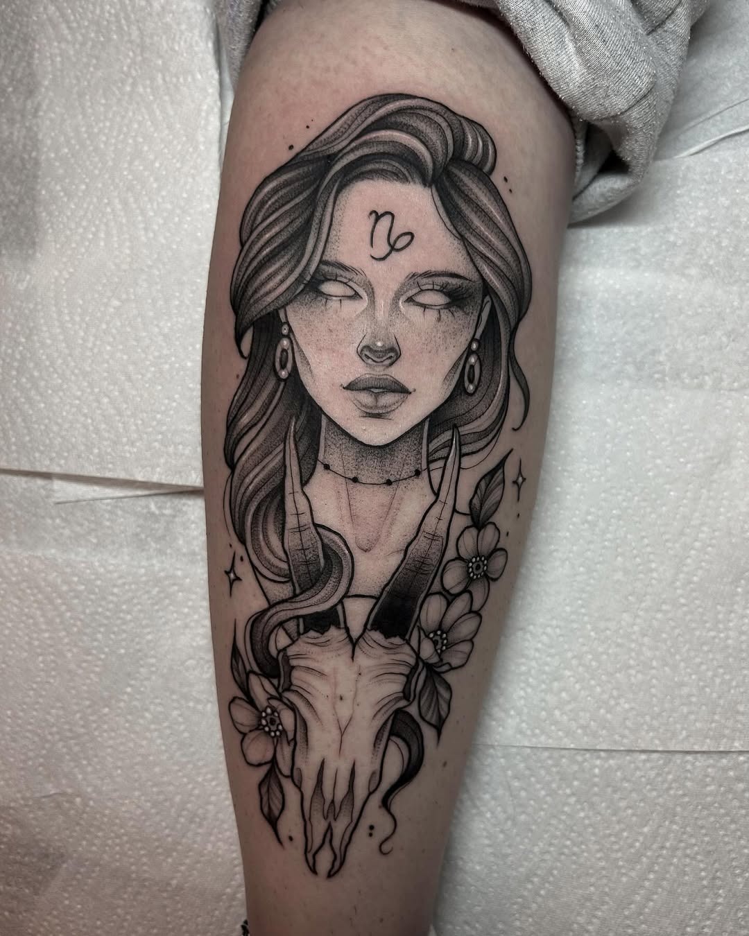 This striking tattoo features a woman with a Capricorn skull and delicate flowers.
