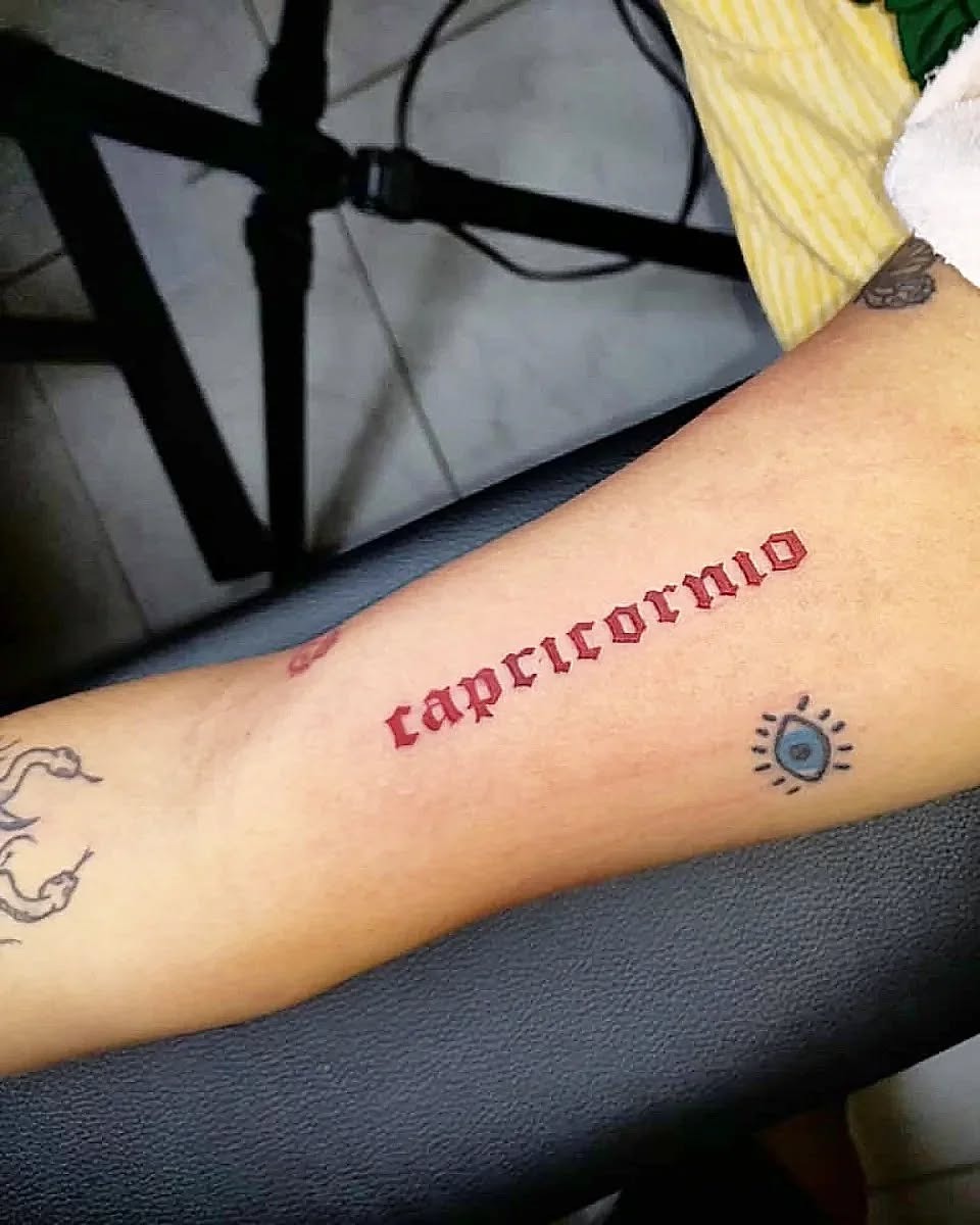 This Capricorn tattoo features bold red lettering, adding a striking pop of color.