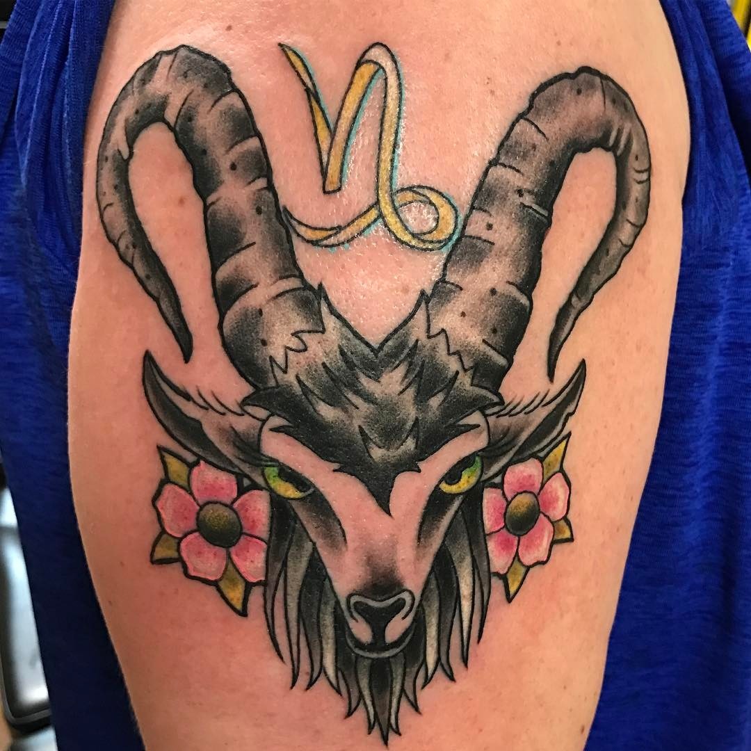 This striking Capricorn tattoo features a fierce goat's head with prominent horns, surrounded by flowers.