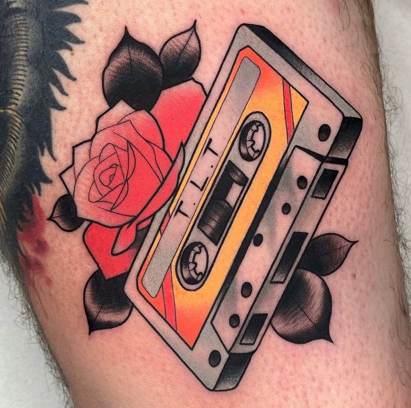 This tattoo features a cassette tape framed by striking roses.