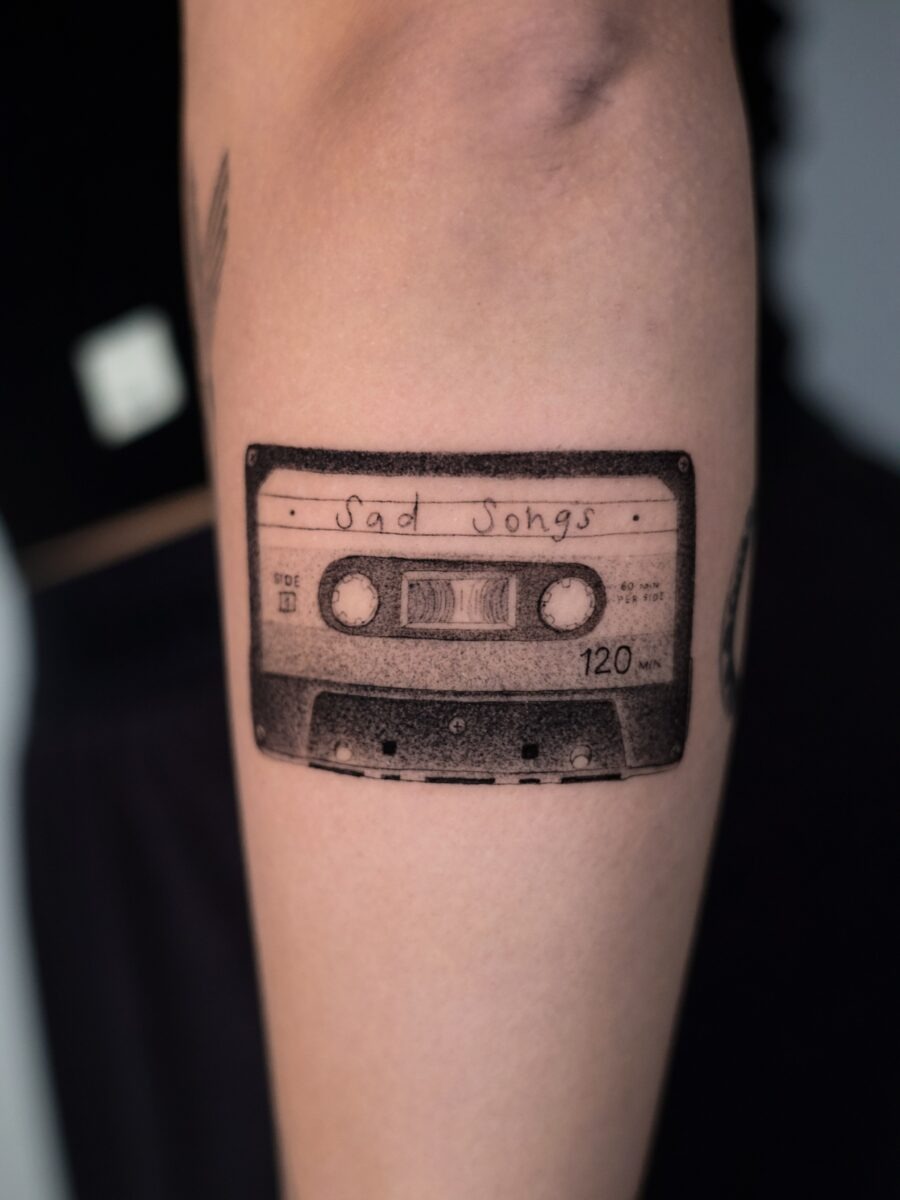 This tattoo features a detailed illustration of a cassette tape labeled 'Sad Songs'.