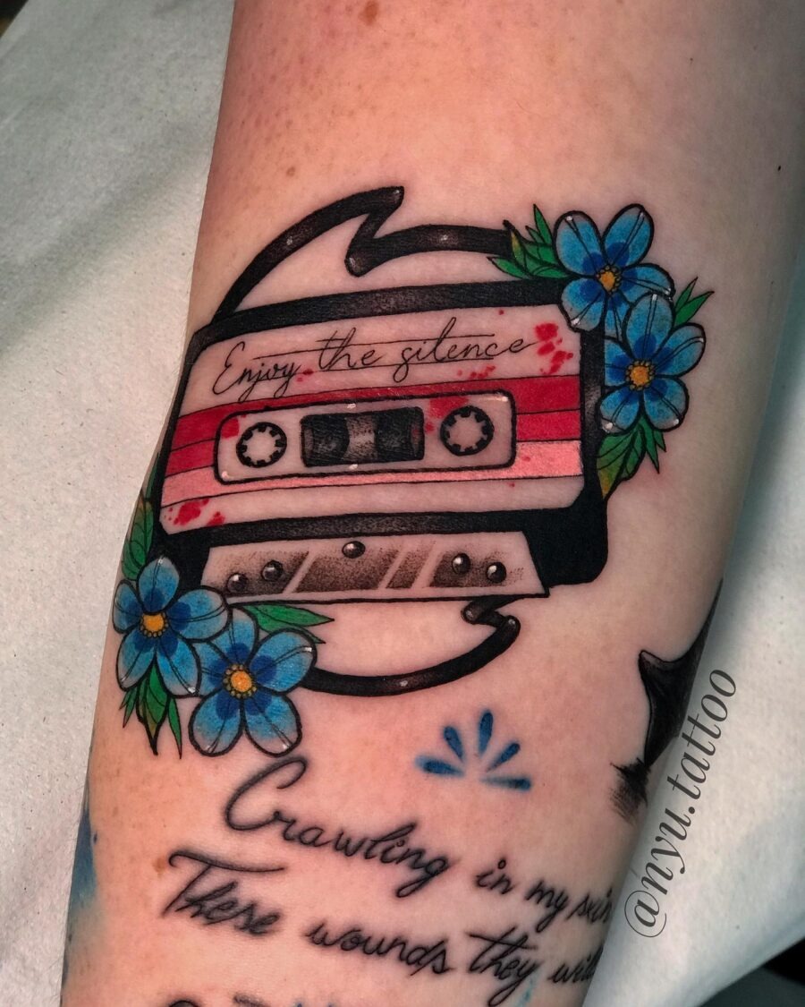 This tattoo features a cassette tape surrounded by blue flowers.